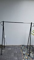 Full view of metal clothing rack with chrome horizontal bar and black legs standing on outdoor stone and rock surface.