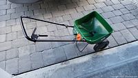 Side view of Scott's Turf Builder Broadcast Spreader showing green hopper, metal handle and wheels.