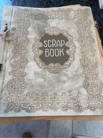 Photo of scrapbook cover labeled 'SCRAP BOOK' with decorative embossed design and string binding.