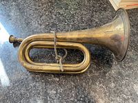 Top down view of antique brass bugle showing curved tubing and flared bell on a granite countertop