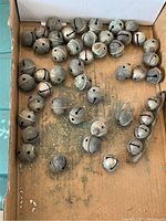 Box containing a large number of antique metal sleigh bells of varying sizes, showing wear and oxidation.
