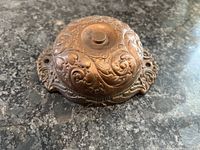 Front view of antique copper door bell showing detailed floral and scrollwork embossing.