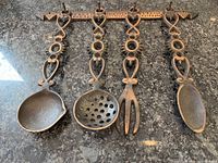 Top view of decorative metal wall hanger with four hanging utensils displayed on textured countertop.