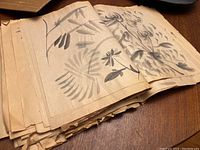 Pile of stacked old ink wash drawings showing floral designs in black ink on aged paper.
