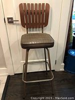 Full front view of the Mid-Century Modern tall stool showing its wooden slat backrest, metal legs, footrest, and worn padded seat.