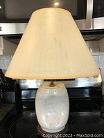 Full view of the lamp showing the beige lampshade and white porcelain base with carved floral designs.