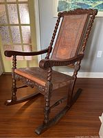 Side and front view of dark wooden rocking chair with intricate carvings on armrests, legs, and seat frame showing overall form and condition.