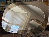 Close-up angled view of the oval mirror showing the reflective surface and beige/champagne curved frame.