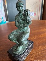 Front view of patinated bronze sculpture of seated woman holding child on black marble base.