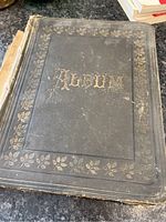 Black Victorian scrap book cover with gold embossed floral border and the word 'Album'