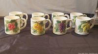 Front view of all six mugs showing the variety of fruit designs including cherries, peach, grapes, and lemons.