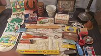 Overview of lot showing assorted vintage advertising rulers, promotional items, fabric souvenir, plaque with horseshoe, tin, and other collectibles on a table