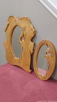 Two carved wooden mirrors with heron motifs, large irregular shaped and smaller oval shape, shown leaning on wall