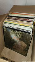 Box of assorted LP vinyl records showing various album covers stacked vertically, highlighting wear and age of covers
