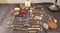 Overview of entire lot showing all spoons, bottle openers, and various collectible advertising items arranged on black cloth surface under lighting.