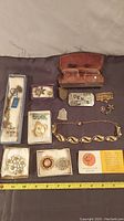Overview photo of all jewelry items laid out including brooches, pins, bracelet, and eyeglasses in case.