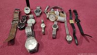 Photo showing all 12 vintage wristwatches of various styles arranged on a red surface.