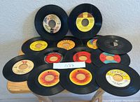 Thirteen 45 RPM vinyl records with various artist labels, arranged on a wooden surface.