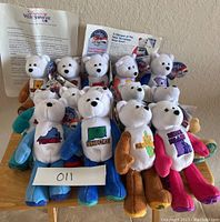 Photo showing a group of 15 collectible plush quarter state bears from Americas Value Showcase, arranged with tags and informational papers visible, featuring several states embroidered on their chests and corresponding state quarters sewn onto one foot.