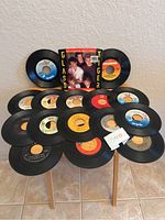 Photo showing all 16 vinyl records, one with a Glass Tiger picture sleeve, the rest are loose black vinyl records.