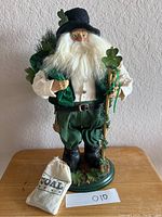Front view of the 19 inch tall Irish Saint Nick figurine with beard, green outfit, holding a staff, standing on a green base, with a small bag labeled 'Coal' placed nearby.