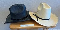 Two cowboy hats, black and white, placed on a wooden bench for size and condition display