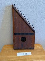Full view of the wooden antique American zither showing rectangular body, tuning pegs, strings, and wear on the wood surface.