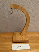 Handmade wooden display stand with curved arm and metal hook, shown from front perspective on wooden surface against a textured wall.
