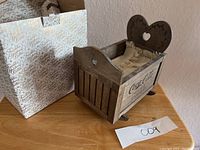 Front angled view of wooden Coca-Cola Franklin Mint doll cradle with original box behind.