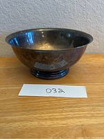 Side view of a rounded silver plate bowl with tarnish on surface, showing reflective metal with darkened areas.