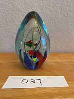Front view showing colorful fish figures inside glass paperweight with blue gradient top and multicolor base design