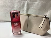 Photo of Shiseido Ultimune serum bottle standing next to the beige faux leather pouch on a white surface.