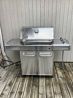 Front view of stainless steel Weber Genesis grill on wood deck
