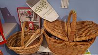 Large wicker picnic basket and smaller wicker basket with wooden utensils inside, displayed on shelf