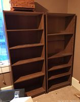Two laminate 5-shelf bookcases standing side by side against a brown wall near a window, showing front and side views.