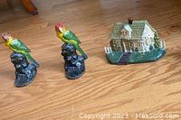 Three painted cast iron doorstops: two parrots on black bases and one house.