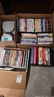 Top view of multiple boxes containing DVDs, showing a large variety of movie and TV series DVDs stacked in cardboard boxes on a carpeted floor.