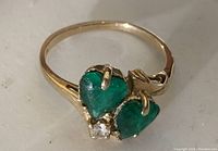 Top-down close-up of 10 kt gold ring showing two heart-shaped green stones and one small clear stone.