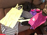 Five items of women's activewear laid out on brown couch including yellow tank top, striped tank top, purple and pink tank top, black zip-up top, and Nike shorts.
