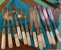 12-piece fish flatware set laid out, showing mother-of-pearl handles, silverplate engraved handles, six forks and six knives