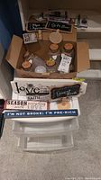 Photo of plastic storage organizer with multiple drawers, assorted wooden signs with printed motivational quotes, and various glass jars with cork stoppers inside the organizer.