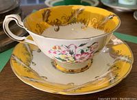Side view showing teacup and saucer with floral and gold designs on yellow background.