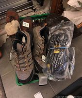 Mixed pair of Merrell hiking shoes with brown and black mesh upper and Vibram soles along with two packaged winter Maxx Dry Grip-ons in sizes L and XL, placed together in a green tote basket.