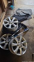 Four Mazda 10-spoke alloy car rims, Subaru rubber and carpeted car mats, and two car brushes on garage floor.