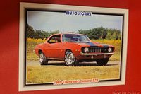 Front of the collectible card showing a red 1969 Chevrolet Camaro Z28 muscle car parked outdoors on grass with clear sky background.