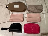 Six designer cosmetic bags on tiled floor showing various sizes and colors