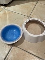 White outer stand and detachable blue inner bowl separated, showing the blue inner bowl with a gel-like texture that can be frozen.