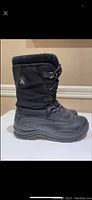 Side profile of single black Kamik women's winter boot showing waterproof material, lace system, and faux fur collar.