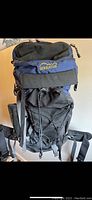 Front view of Serratus backpack in black and navy with yellow logo, showing front bungee cord pocket and adjustable straps.