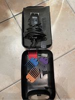 Photo of Wahl dog grooming clipper set showing clipper with coiled cord, black comb, multiple colored clipper guard attachments, small accessory, all inside black plastic carrying case.